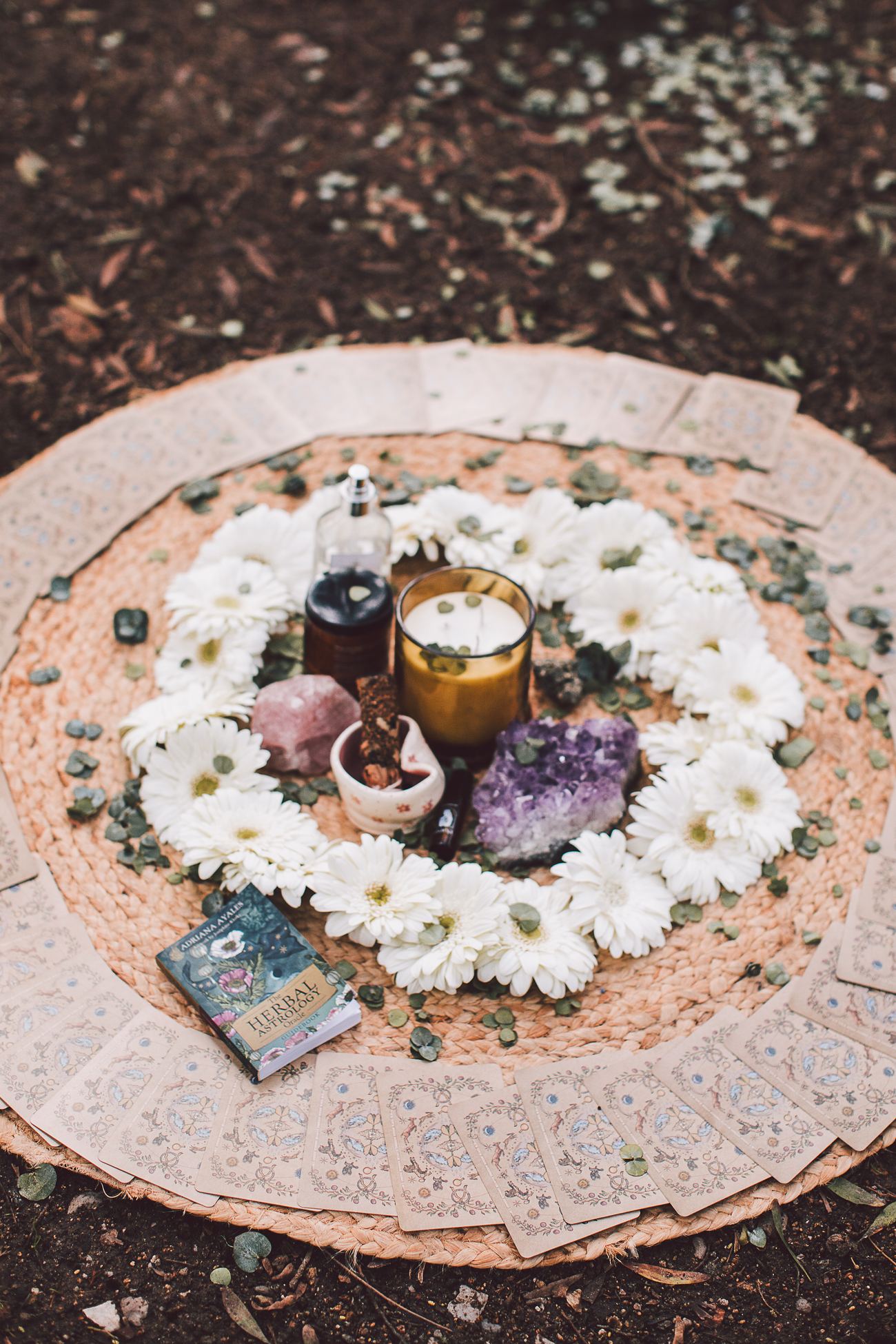 A circular altar of white flowers, candles, oils and crystals on the forest floor