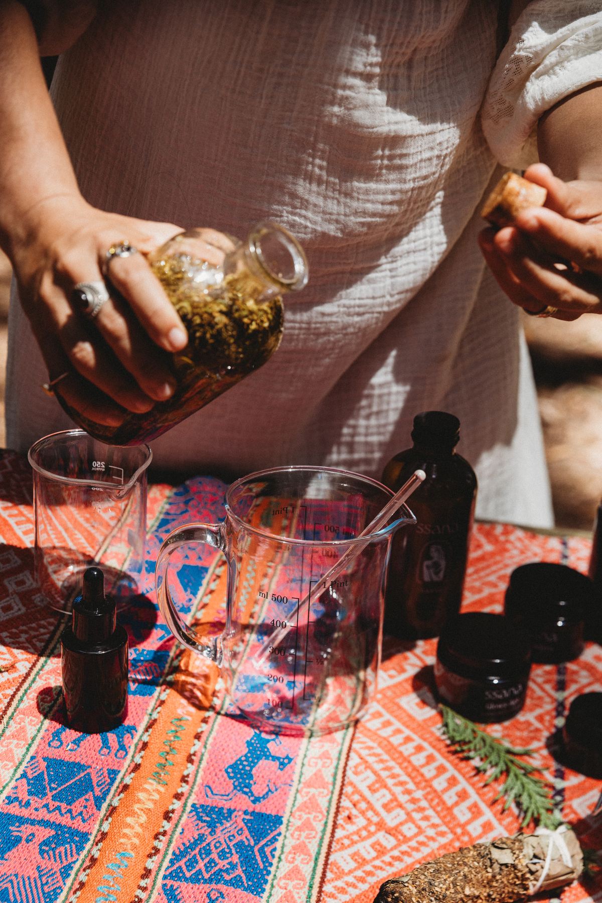 Hands pouring a golden infused herbal oil into a glass measure