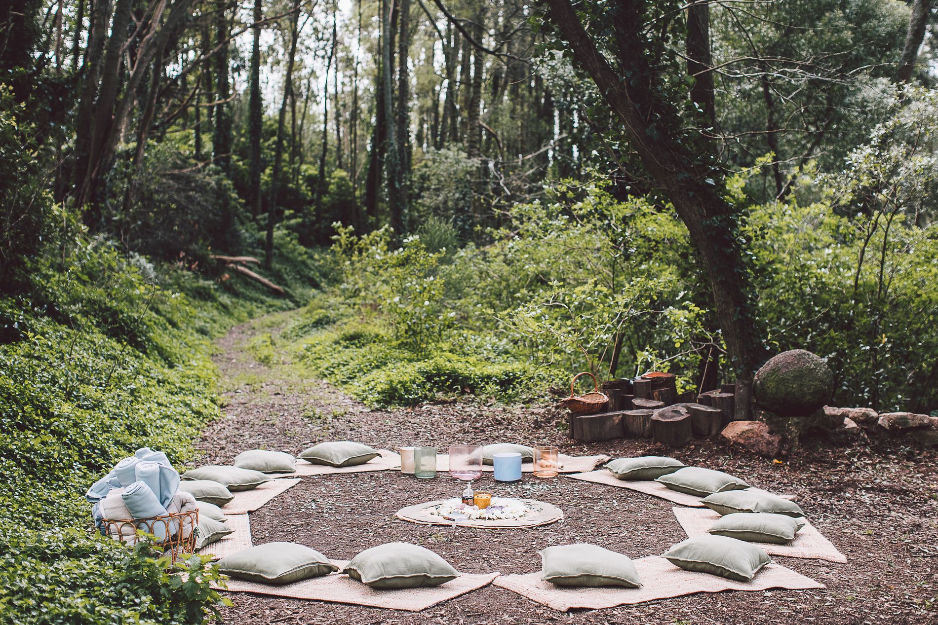 A circle of cushions and blankets laid out on the forest floor, waiting